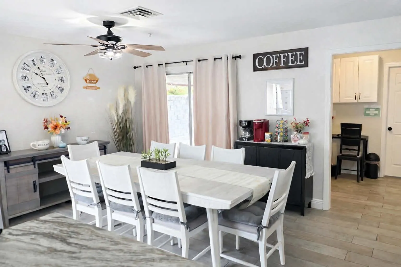 The long white dining table at Latham set with eight cushioned chairs, beside a coffee station and a door to the patio