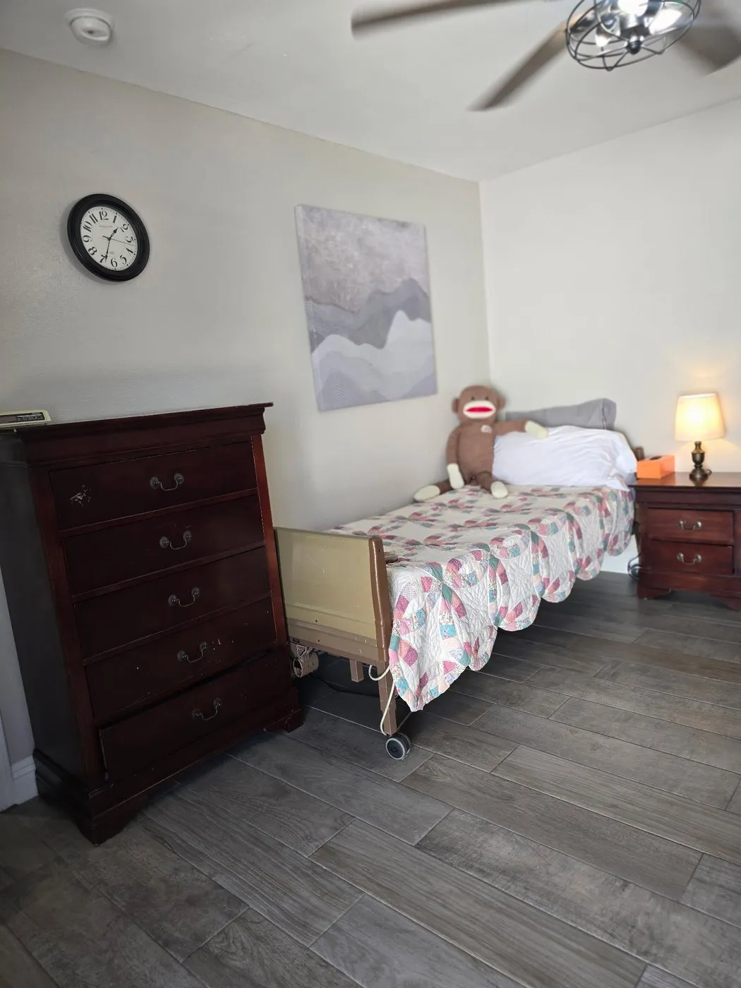 A resident bedroom at Latham with a patchwork quilt on the bed, a tall dresser, and a wall clock