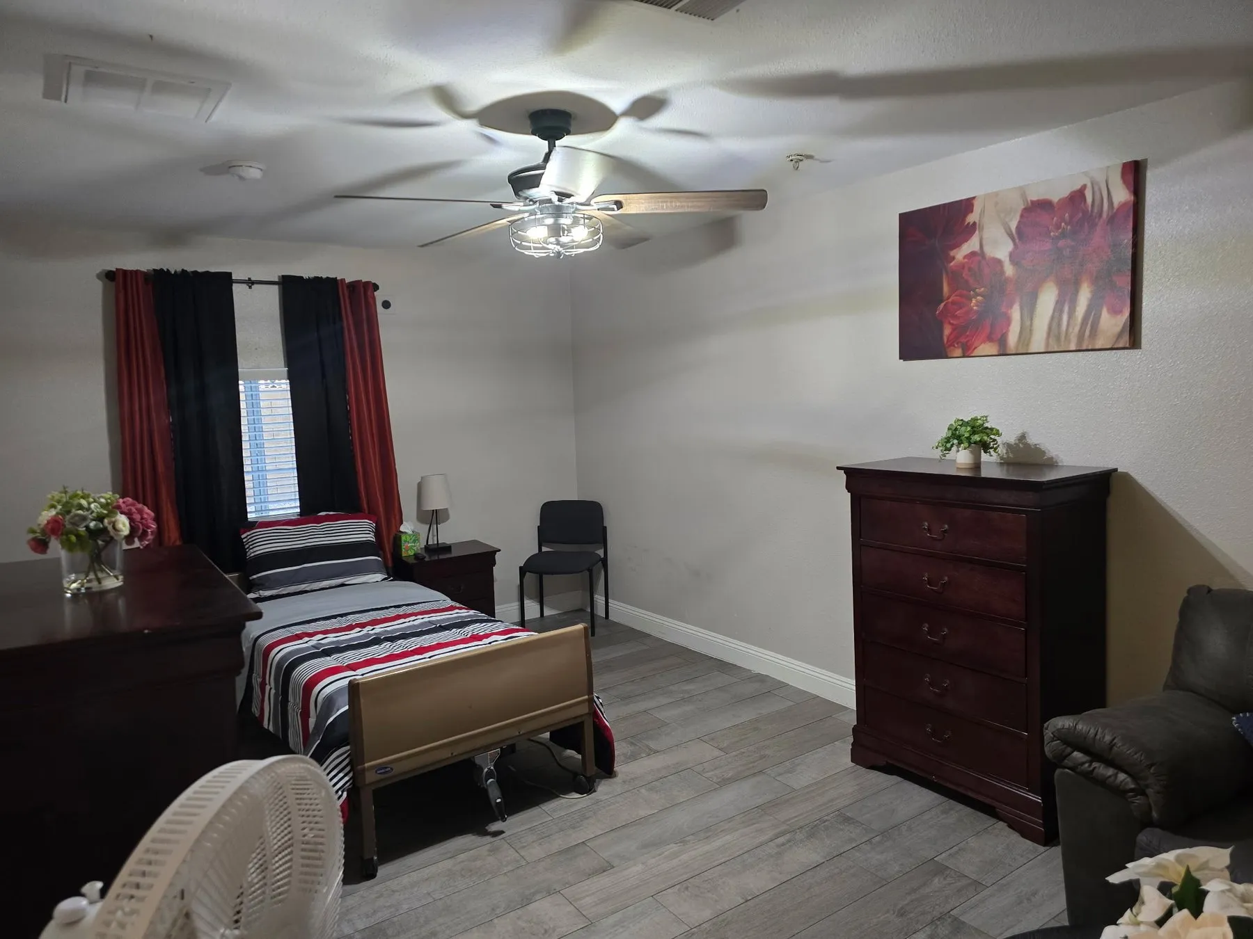 A resident room at Latham with an adjustable care bed, a wooden dresser, and a recliner beside the window