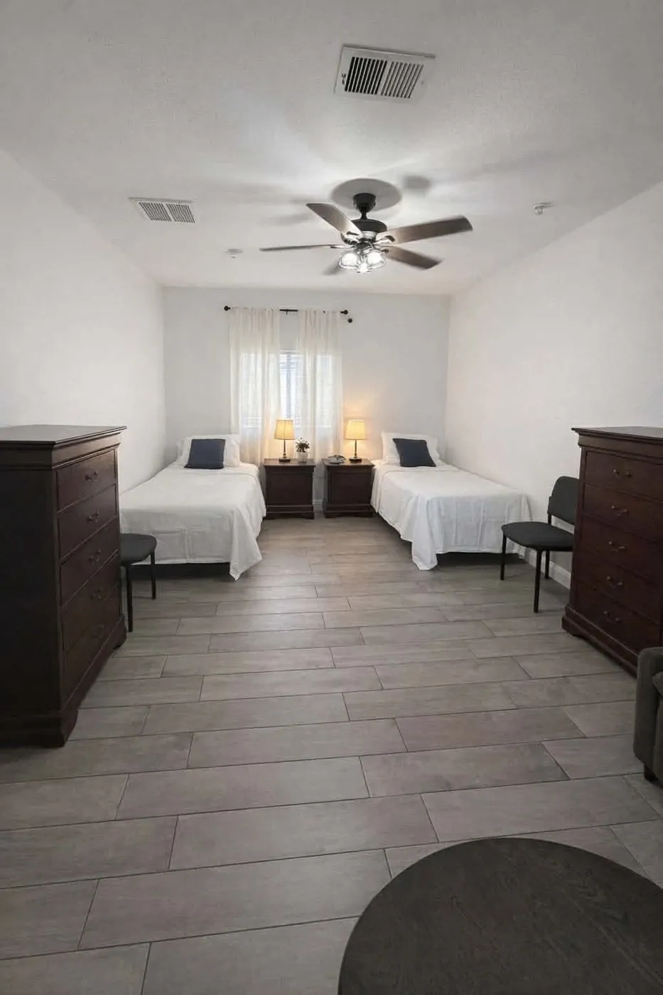 A spacious shared bedroom at Latham with two twin beds, matching bedside lamps, and a dresser for each resident